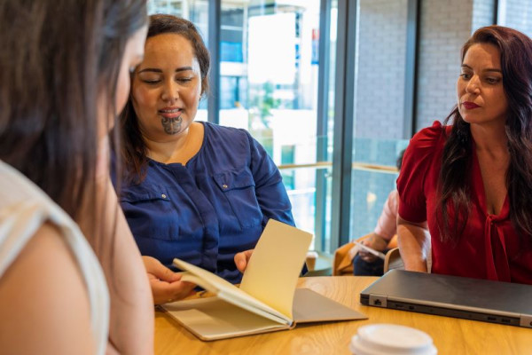 Three people sitting around a table looking at a notebook